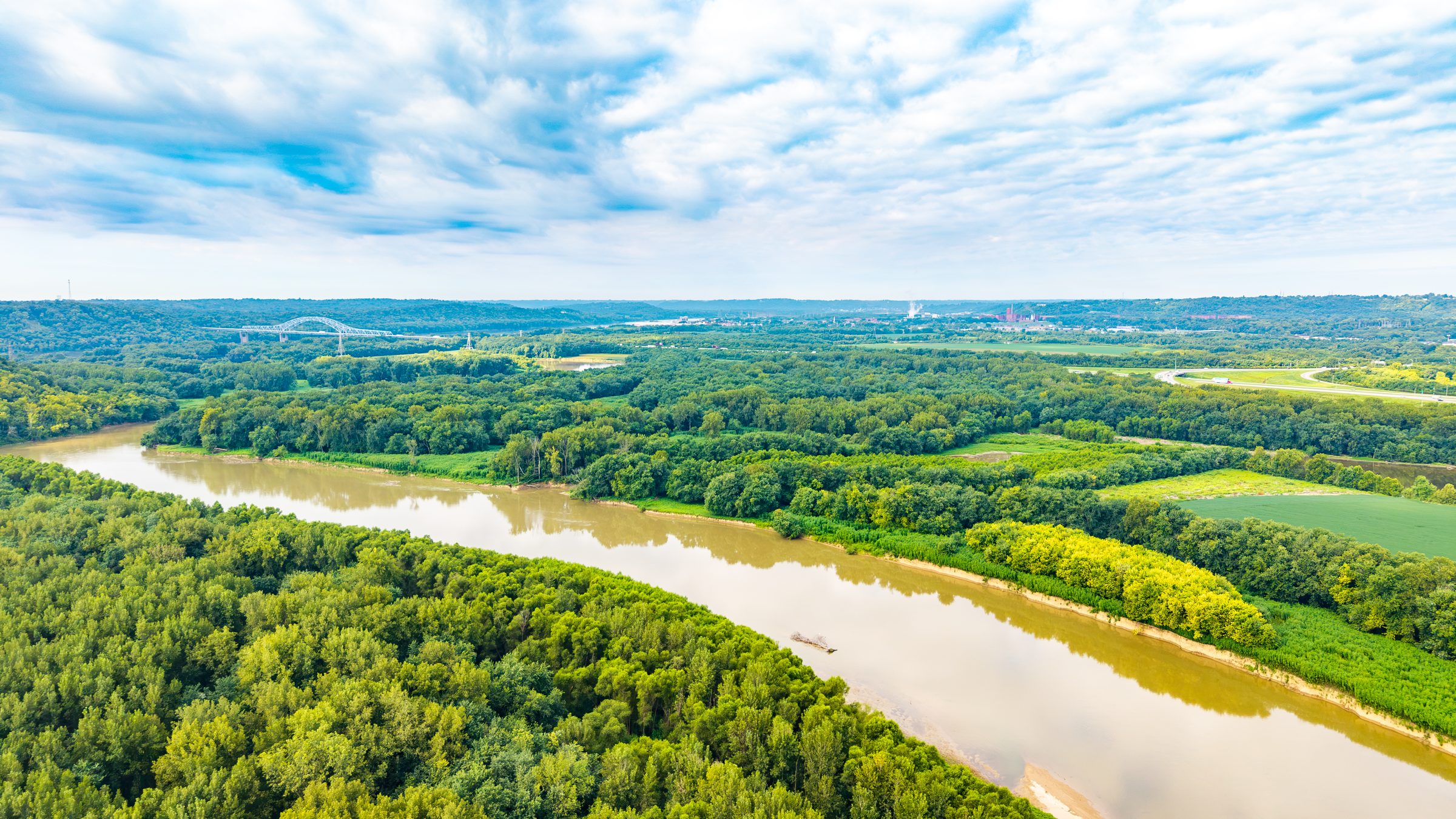 Aerial view of the river curving through green floodplain forest under a wide cloudy sky
