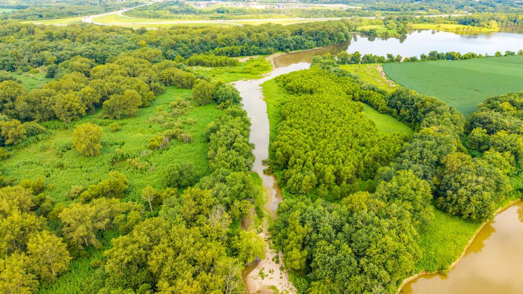 Aerial view of a narrow channel winding through dense green woods toward the river