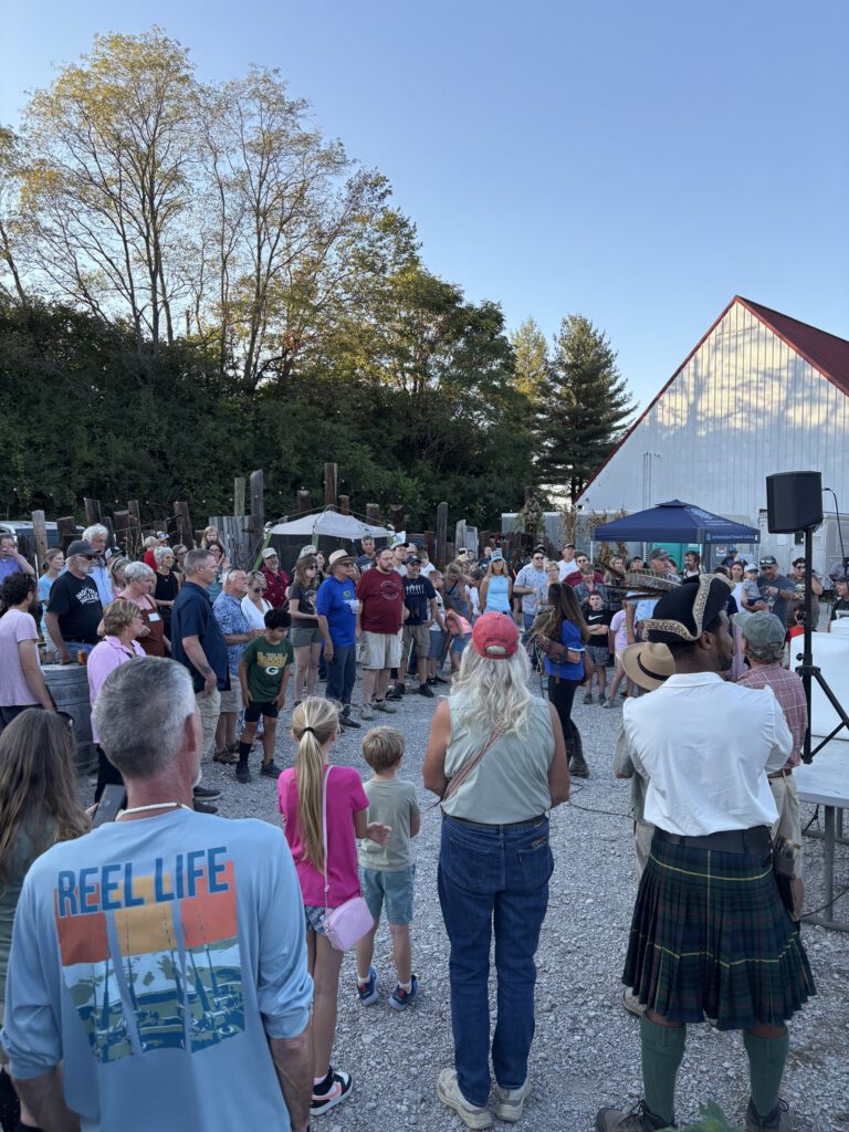 Festival crowd gathered on gravel in front of a white barn at dusk