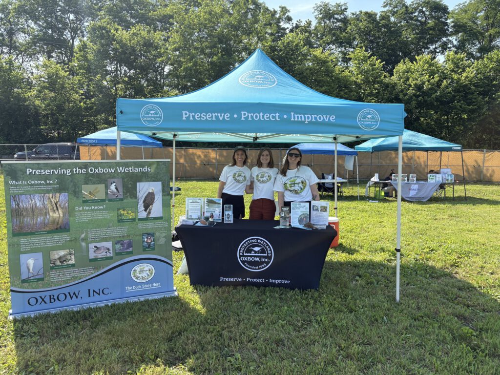 Oxbow staff at the outreach tent beside the "Preserving the Oxbow Wetlands" banner